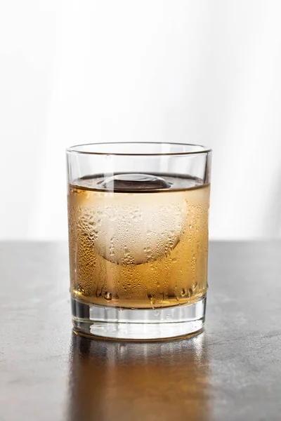 Vidrio húmedo con whisky fuerte y cubo de hielo en blanco - foto de stock