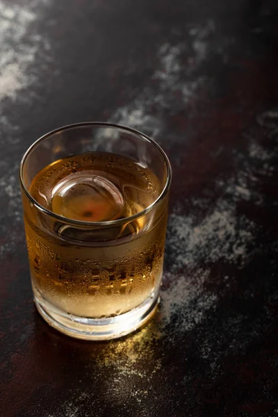 Glass with strong whiskey and ice cube on black surface — Stock Photo