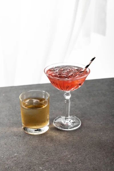 Glass with whiskey near red cosmopolitan cocktail and straw on white — Stock Photo