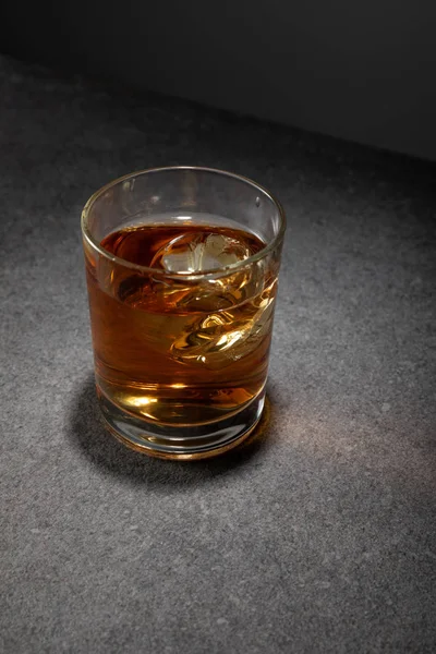 Ice cubes in glass of brandy on grey surface — Stock Photo