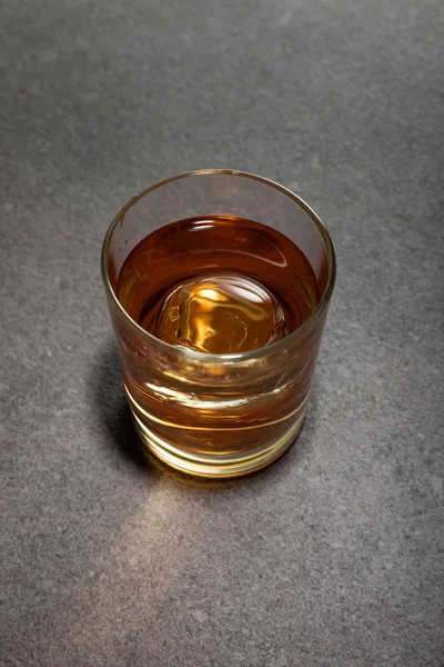 Top view of ice cube in glass of brandy on grey surface — Stock Photo