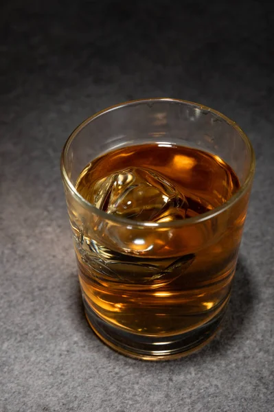 Cubitos de hielo en vaso de bebida alcohólica sobre superficie gris - foto de stock