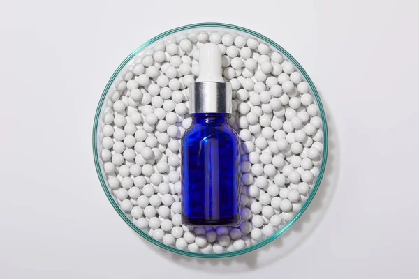 Top view of blue bottle of oil on decorative beads in laboratory glassware on white background — Stock Photo