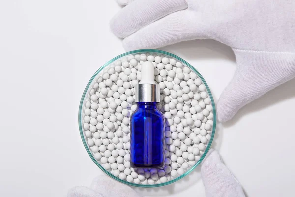 Cropped view of man holding laboratory glassware with blue bottle of oil on decorative beads on white background — Stock Photo