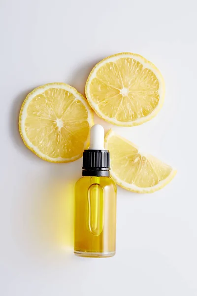 Vista superior de la botella de aceite cosmético con rodajas de limón sobre fondo blanco - foto de stock