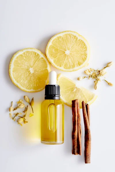 Vista dall'alto della bottiglia di olio cosmetico con fette di limone, bastoncini di cannella e boccioli di vaniglia su sfondo bianco — Foto stock