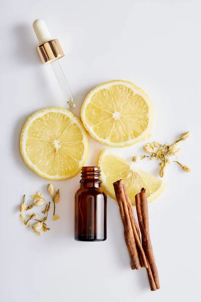 Vista superior da garrafa de óleo cosmético com conta-gotas, fatias de limão, paus de canela e botões de baunilha no fundo branco — Fotografia de Stock