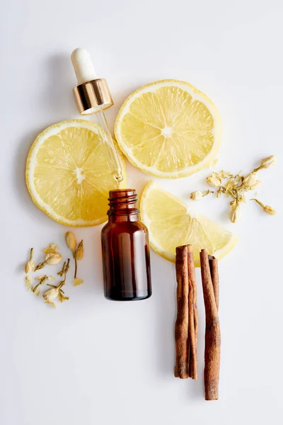 Vista superior da garrafa de óleo cosmético com conta-gotas, fatias de limão, paus de canela e botões de baunilha no fundo branco — Fotografia de Stock