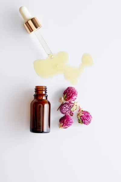 Vista superior del aceite cosmético que sale del gotero junto a la botella y los brotes de color rosa sobre fondo blanco - foto de stock