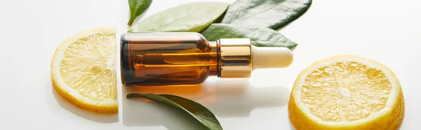 Top view of bottle of cosmetic oil with leaves and slices of lemon on white background, panoramic shot — Stock Photo