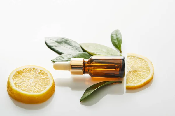 Vista superior de la botella de aceite cosmético con hojas y rodajas de limón sobre fondo blanco, plano panorámico - foto de stock
