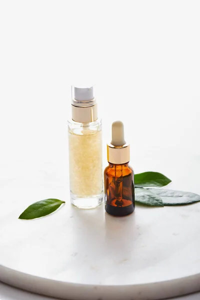 Bottles of cosmetic oil with leaves on round stand isolated on white — Stock Photo