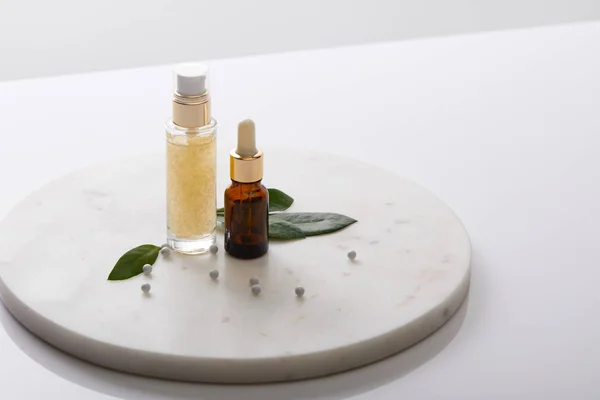 Bottles of cosmetic oil with leaves and decorative beads on round stand isolated on grey — Stock Photo