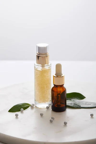 Bottiglie di olio cosmetico con foglie e palline decorative su cavalletto rotondo isolato su grigio — Foto stock