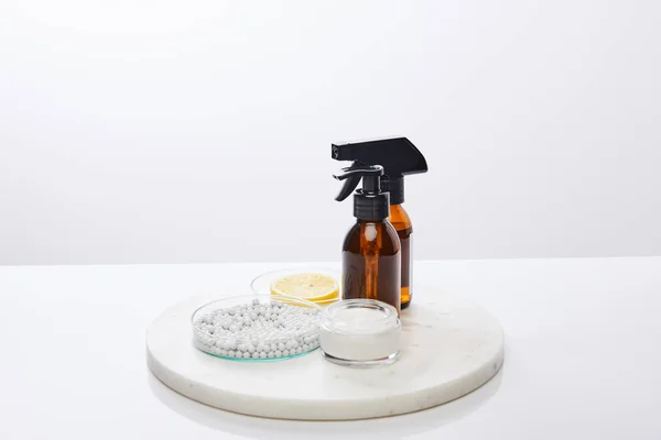 Bottles of oil, cosmetic cream and laboratory glassware with decorative beads, slice of lemon isolated on grey — Stock Photo