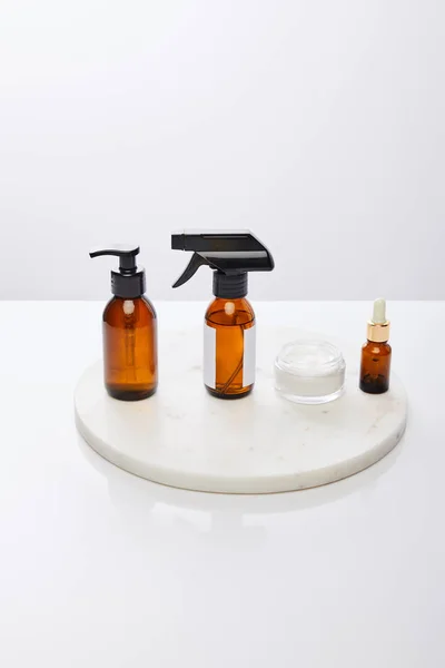 Dispenser bottles of oil next to cosmetic cream on round stand isolated on grey — Stock Photo