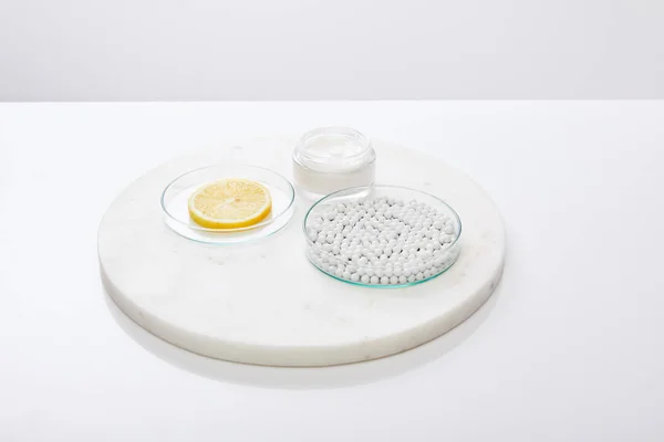 Artículos de vidrio de laboratorio con cuentas decorativas, rodaja de limón con crema cosmética en soporte redondo aislado en gris — Stock Photo