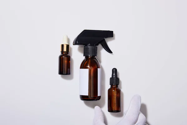 Vista recortada de mano en guante con dispensador botellas cosméticas de aceite sobre fondo gris — Stock Photo