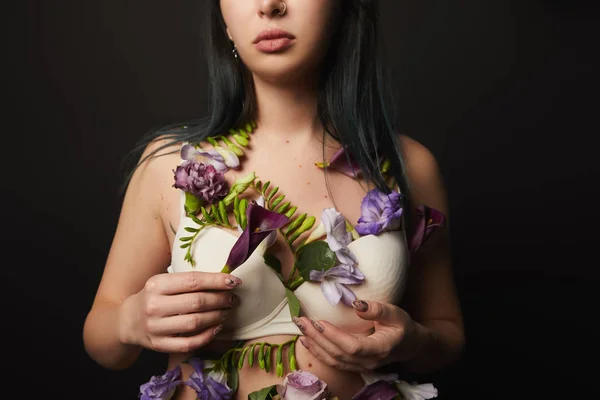 Vista ritagliata di bella ragazza in reggiseno con fiori viola e viola sul corpo isolato su nero — Foto stock