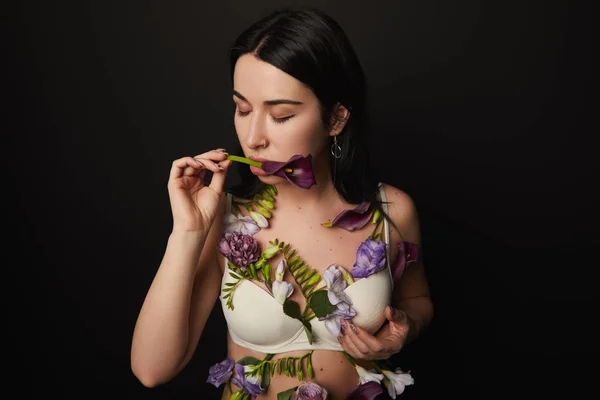 Beautiful girl in bra with closed eyes and violet and purple flowers on body isolated on black — Stock Photo