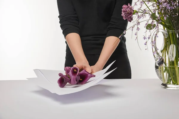 Vista recortada de floristería envolviendo flores de cala púrpura en papel aislado en blanco - foto de stock