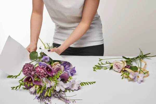 Vue recadrée du fleuriste enveloppant bouquet violet dans du papier isolé sur blanc — Photo de stock