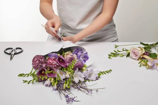 Vue recadrée du fleuriste enveloppant bouquet violet dans du papier isolé sur blanc — Photo de stock