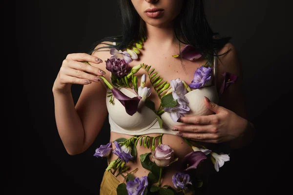 Vue recadrée de fille en soutien-gorge avec des fleurs violettes et violettes sur le corps isolé sur noir — Photo de stock