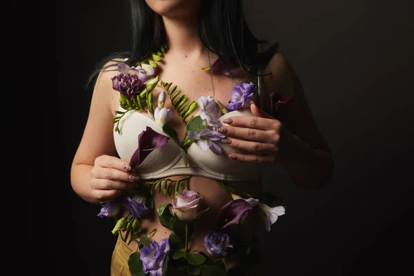 Vue recadrée de fille en soutien-gorge avec des fleurs violettes et violettes sur le corps isolé sur noir — Photo de stock