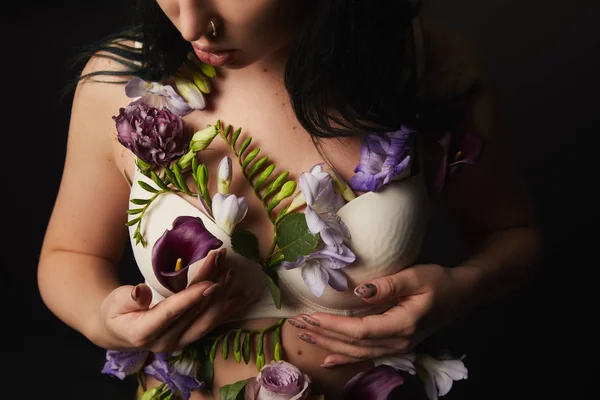 Vue recadrée de fille en soutien-gorge avec des fleurs violettes et violettes sur le corps isolé sur noir — Photo de stock