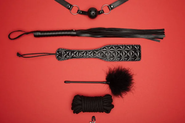 Верхний вид черной весло, кляп, веревка, перо щекотун и порка кнут изолированы на красный — стоковое фото