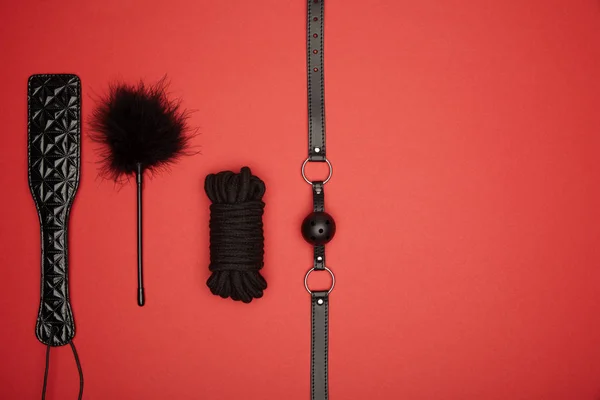 Top view of black paddle, gag, rope, feather tickler isolated on red — Stock Photo