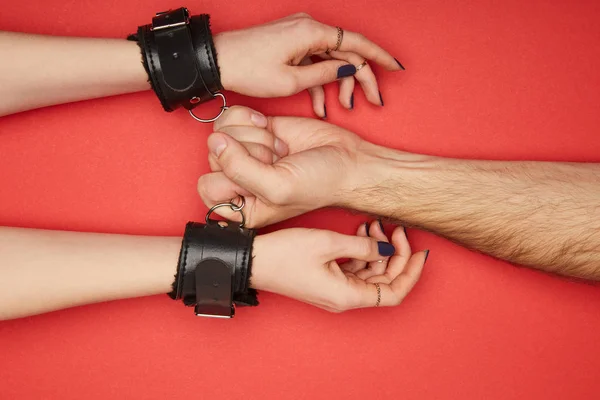 Обрізаний вид чоловіка, який тримає наручники на жінці ізольовані на червоному — стокове фото