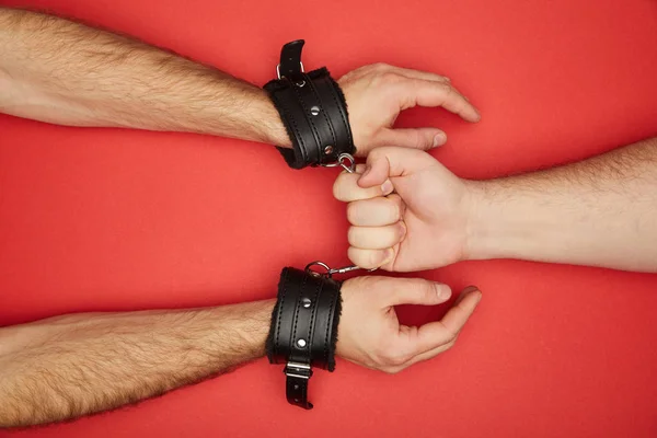 Cropped view of man holding handcuffs on man isolated on red — Stock Photo
