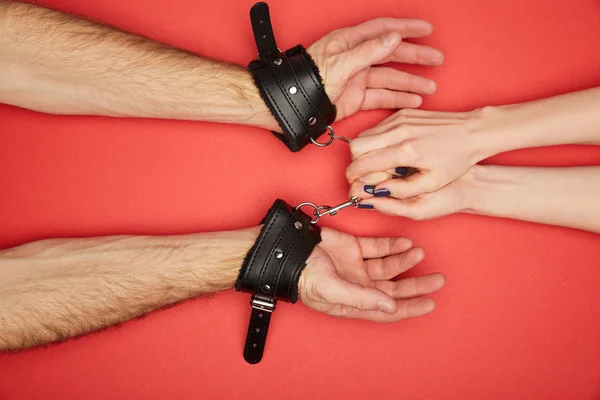 Cropped view of woman holding handcuffs on man isolated on red — Stock Photo