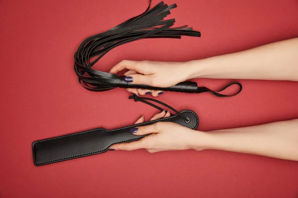 Cropped view of woman with paddle and flogging whip isolated on red — Stock Photo