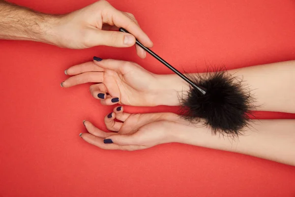 Cropped view of man tickling female hands with feather tickler isolated on red — Stock Photo