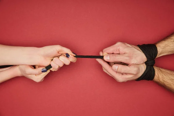 Corte vista de mulher segurando corda em amarrado mãos masculinas isoladas no vermelho — Fotografia de Stock