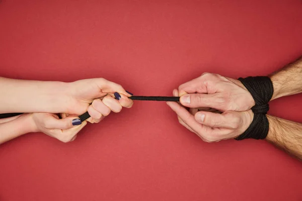 Cropped view of woman holding rope on tied male hands isolated on red — Stock Photo