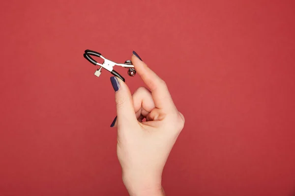 Cropped view of woman holding nipple clamp isolated on red — Stock Photo