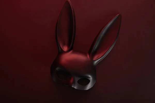 Vue du dessus du masque noir de lapin dans un éclairage sombre sur fond rouge — Photo de stock