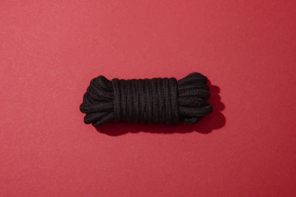 Top view of black rope on red background — Stock Photo