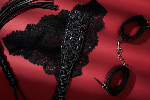 Draufsicht auf schwarze Sexspielzeuge und weibliche Höschen auf rotem Hintergrund — Stockfoto