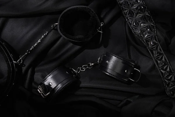 Top view of handcuffs and paddle on black textile background — Stock Photo