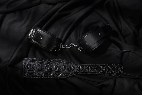 Top view of handcuffs and paddle on black textile background — Stock Photo