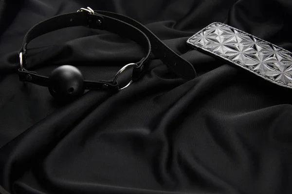 Gag and spanking paddle on black textile background — Stock Photo