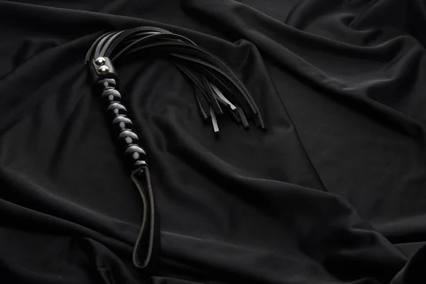 Látigo azotes de cuero sobre fondo textil negro - foto de stock