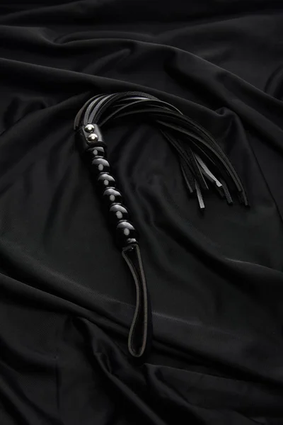 Leather flogging whip on black textile background — Stock Photo