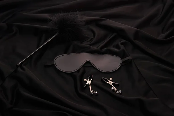 Piuma tickler, maschera e morsetti capezzolo su sfondo tessile nero — Foto stock