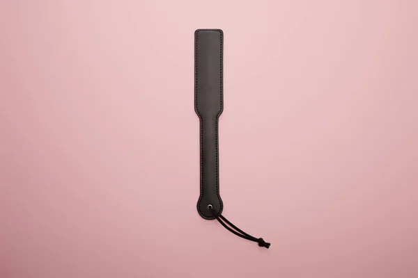 Top view of black spanking paddle on pink background — Stock Photo